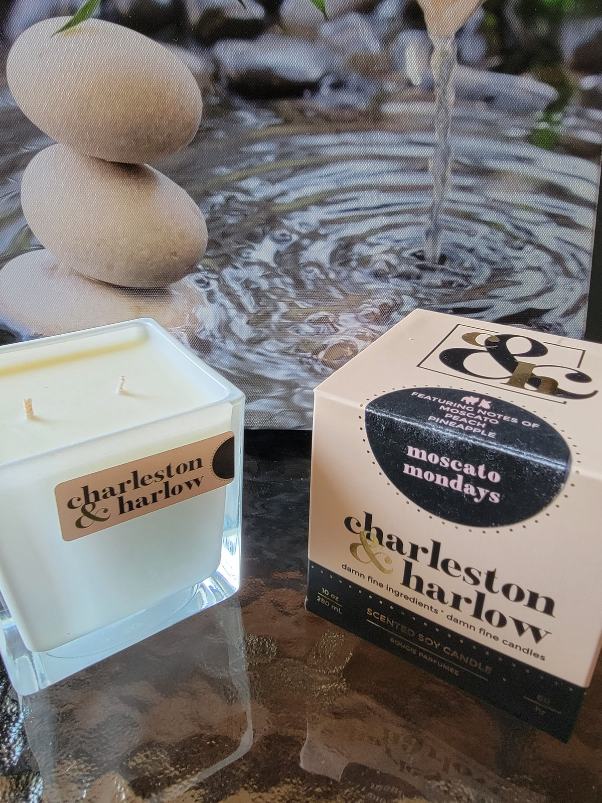 Charlston &amp; Harlow Mosecato  Mondays candle on a table with flowing water and rocks in the background