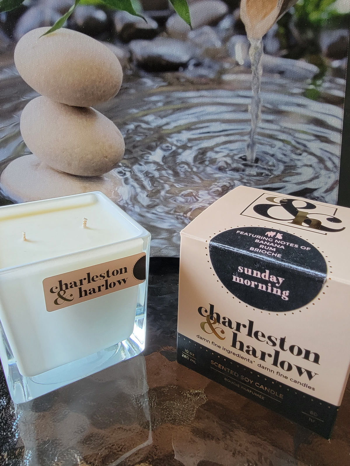 Charlston &amp; Harlow  Sunday Morning  Candle  on a table with flowing water and Rocks in the background